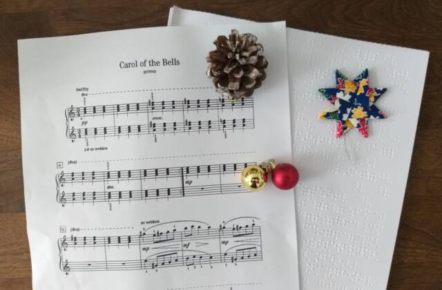 Ein Notenblatt in Schwarzdruck und Braille von "Carol of the Bells" mit einem Tannenzapfen, Glöckchen und einen Weihnachtsstern