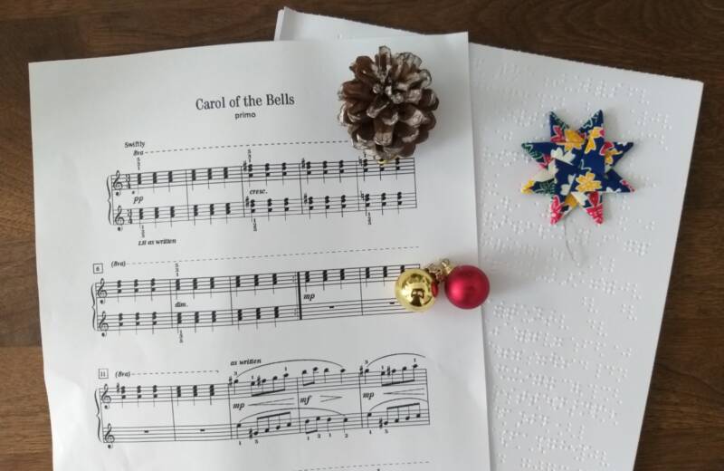 Ein Notenblatt in Schwarzdruck und Braille von "Carol of the Bells" mit einem Tannenzapfen, Glöckchen und einen Weihnachtsstern