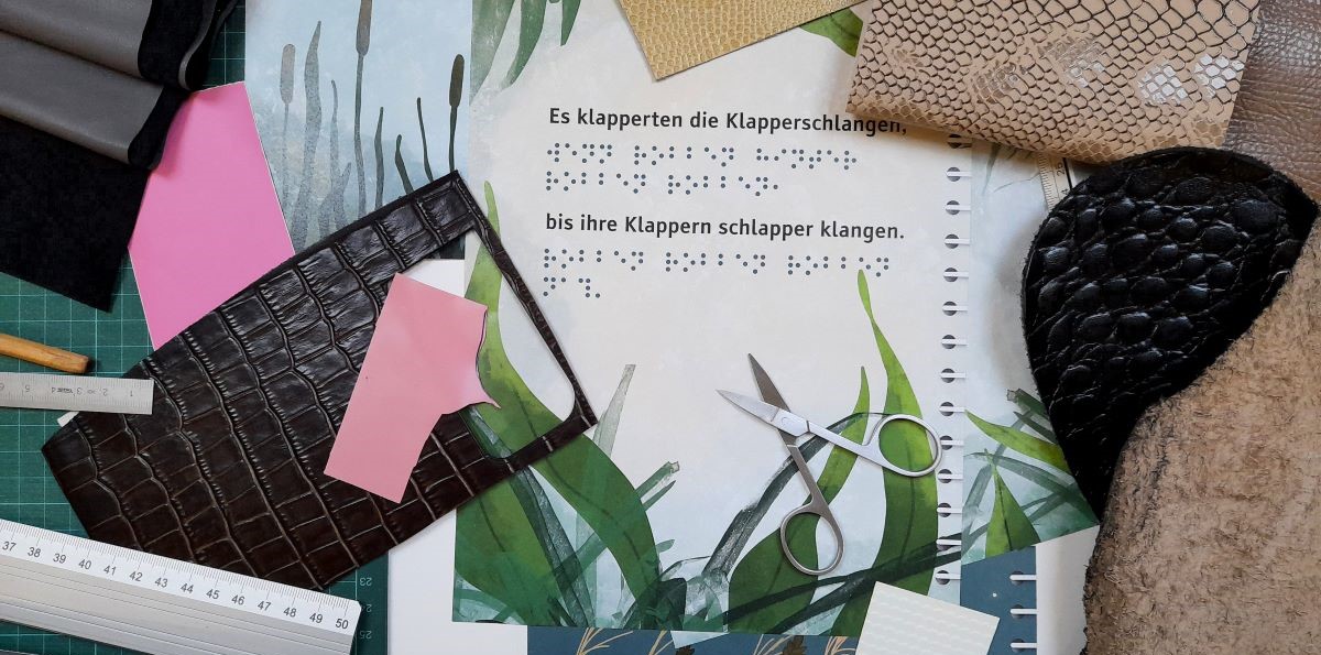 Auf einem Entwurf einer Buchseite liegen verschiedene Materialien Stoffe und Werkzeuge